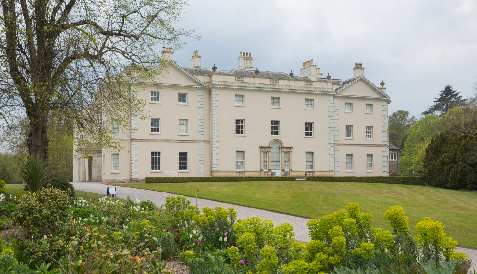 Large white Georgian country house with formal lawns and flower beds in the foreground.